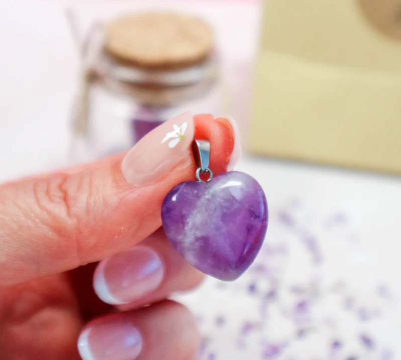 Petit pendentif cœur en améthyste tenu entre les doigts